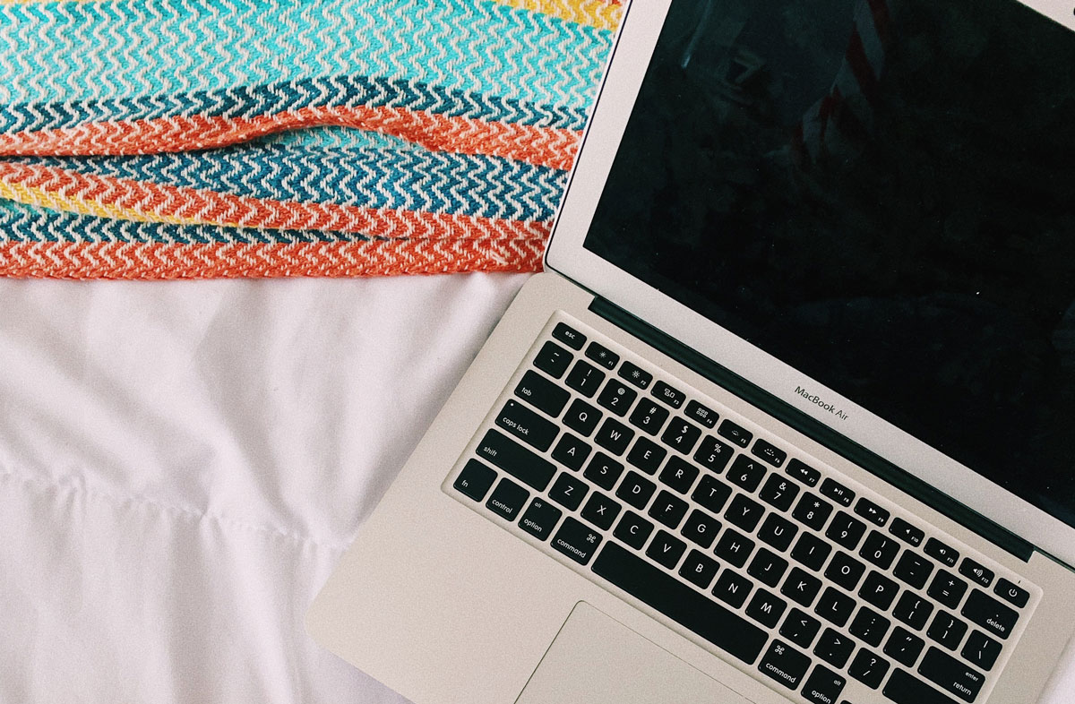 open laptop sitting on white bed sheets and multicolored blanket